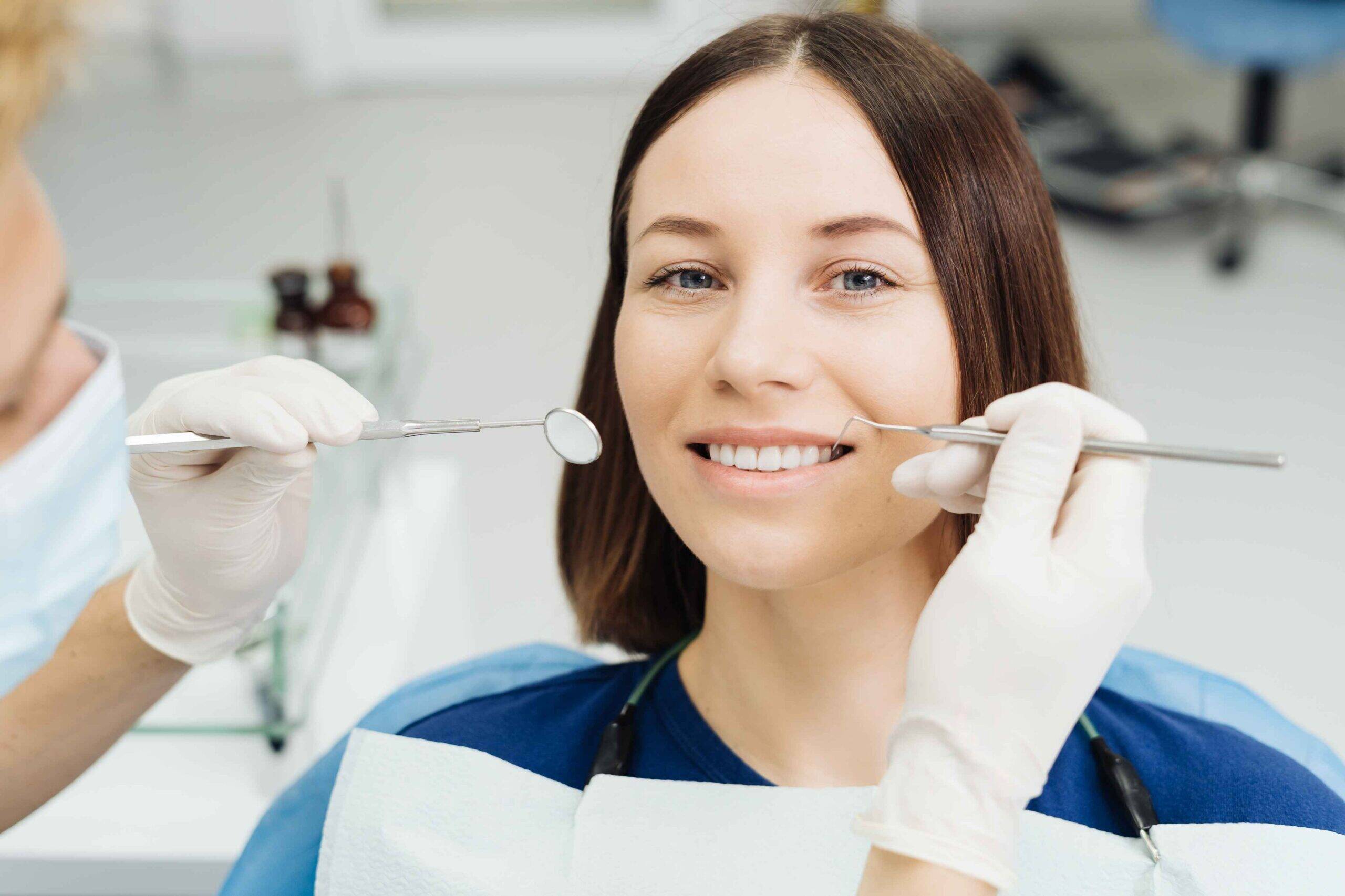 Dentist examining smiling patient's teeth with dental mirror and probe during checkup.