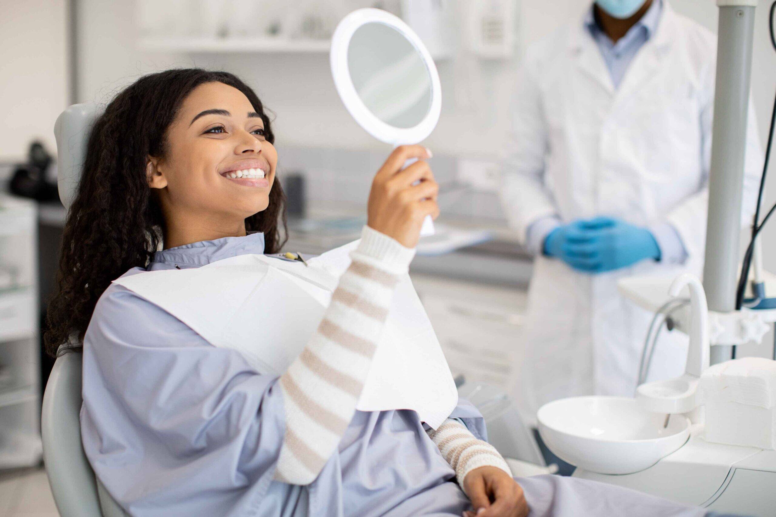 Smiling patient checking her smile in a mirror after dental treatment.