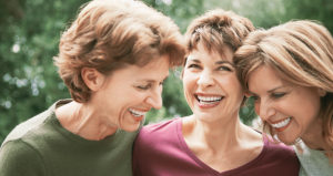 Three middle-aged women smile to reveal their beautiful dental implants